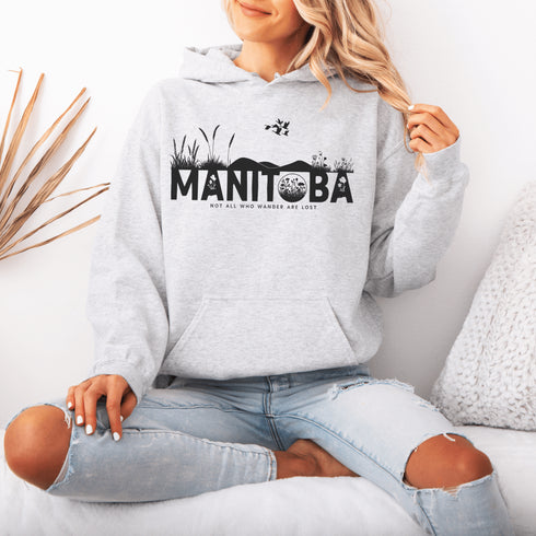 Featuring a prairie landscape, the design showcases wildflowers and prairie grasses blooming from the letters "Manitoba," artfully integrated into the scene.